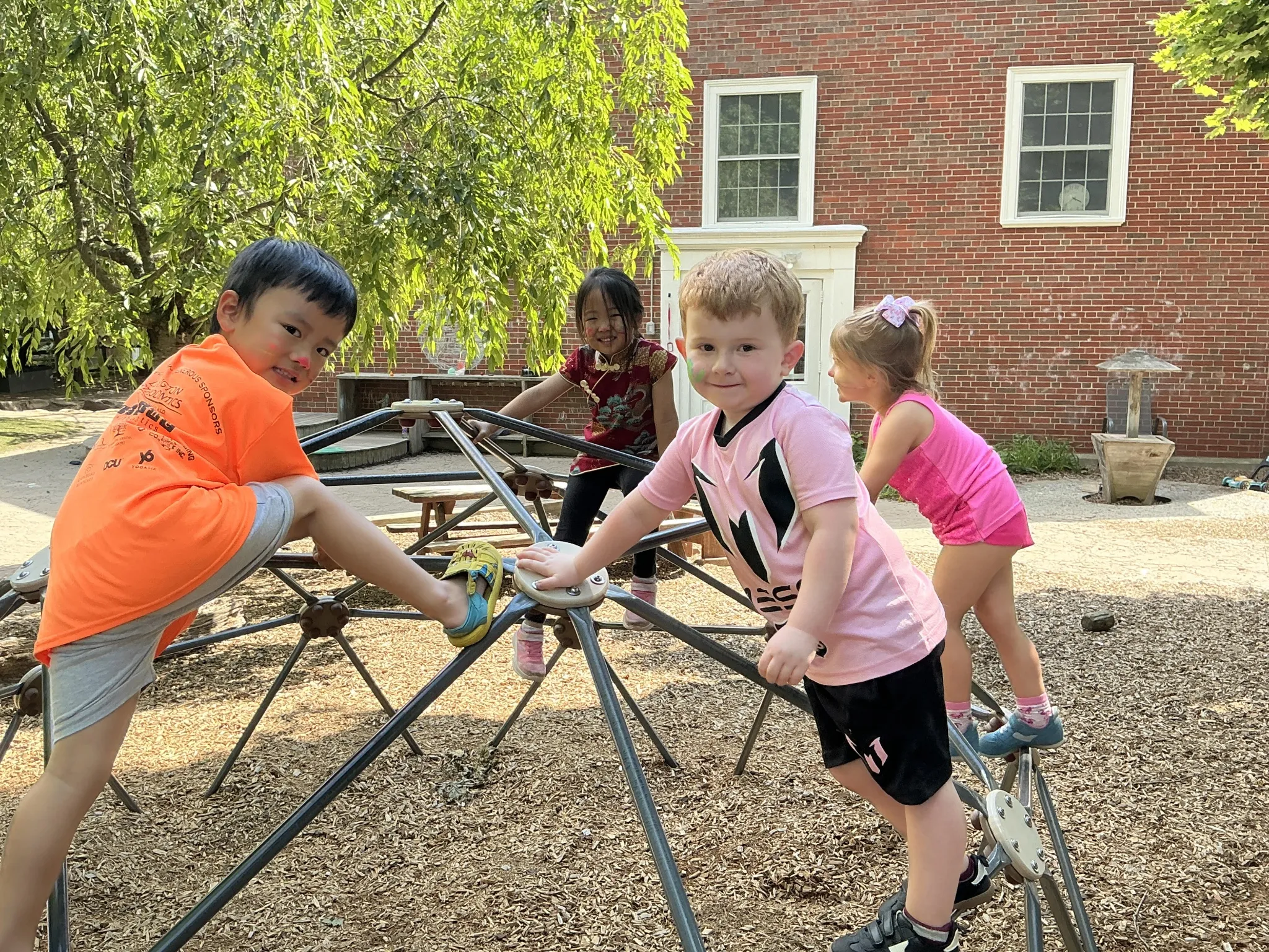 Four preschoolers with face paint climb the dome climber on the LPC playground in Lexington, MA