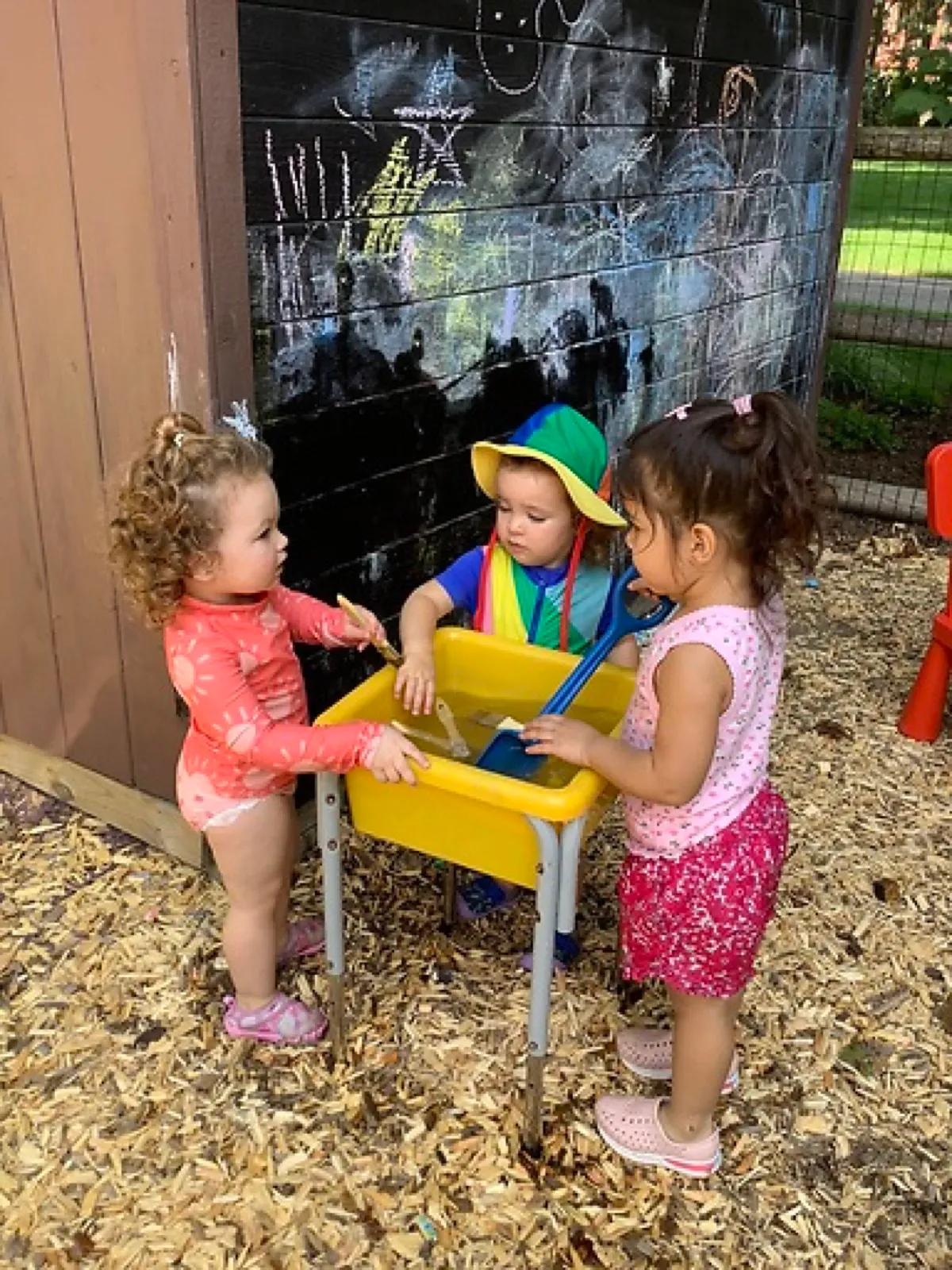Three LPC toddlers scoop and pour together at the outdoor water table