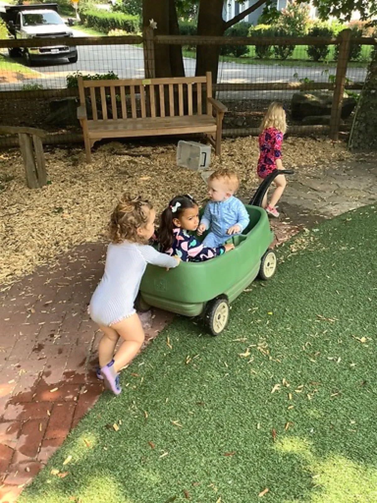 Young children push a friend in a green wagon across the playground