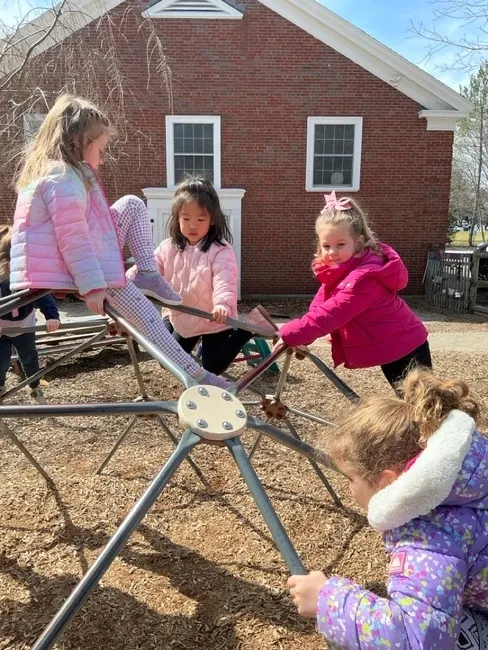 Four children in winter coats climb the dome climber on a bright cold day