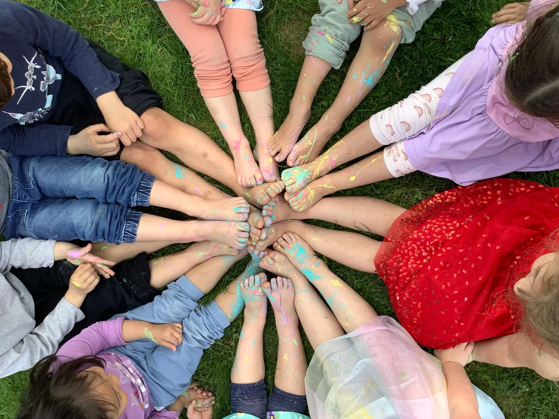 Paint-covered bare feet meet in a sun-ray circle on the grass at LPC
