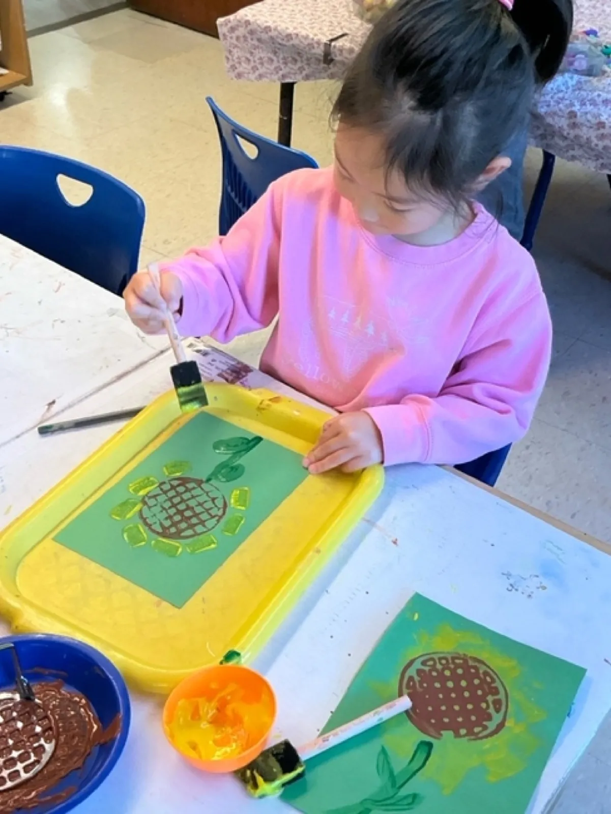 A preschooler sponge-paints a sunflower stencil onto green paper