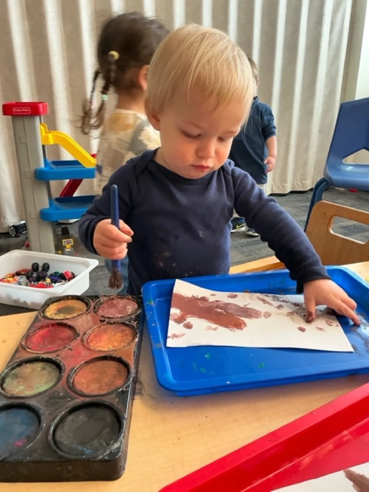 A toddler concentrates on a watercolor painting